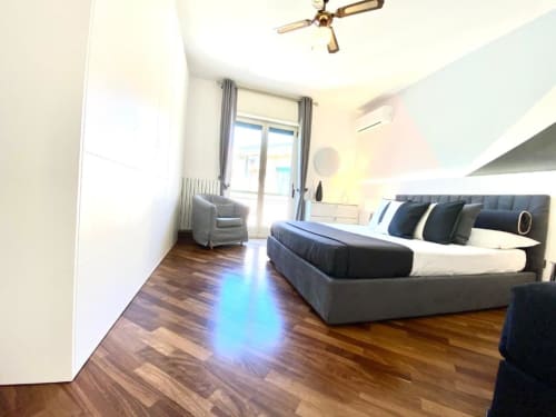 Camera moderna negli Mottola Apartments di Tropea con letto king, poltrona grigia, pavimenti in legno e balcone con vista giardino