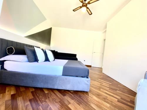 Camera da letto moderna con letto nero, biancheria blu, pavimenti in legno e soffitto inclinato con ventilatore dorato negli Appartamenti Mottola, Tropea
