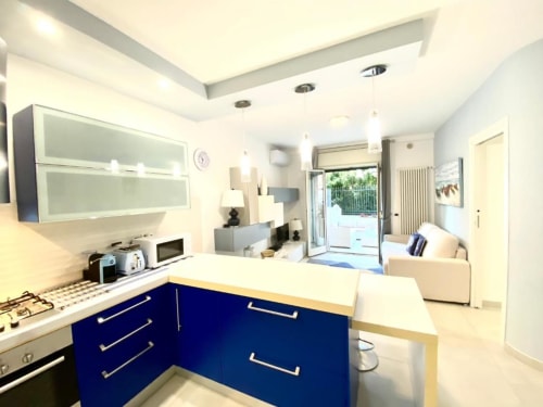 Moderna zona cucina e soggiorno open-plan agli Appartamenti Mottola a Tropea con cabinetry blu, banconi bianchi e accesso a