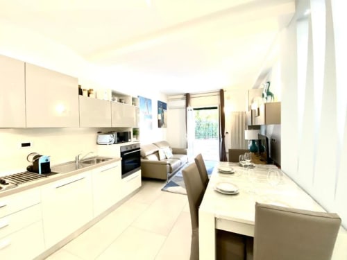 Moderna zona cucina-pranzo negli Appartamenti Deluxe di Mottola, Tropea con mobili bianchi, tavolo da pranzo e vista sul giardino