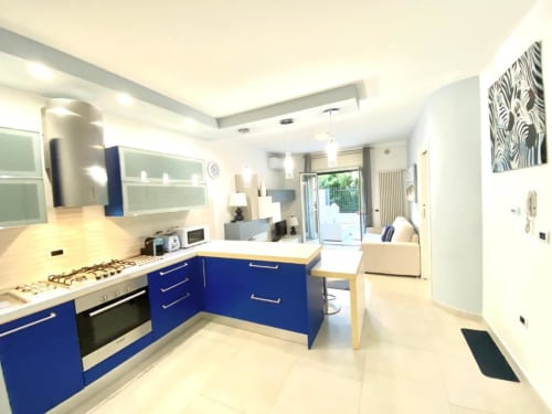 Cucina moderna con mobili blu e piani bianchi negli Appartamenti Mottola, Tropea. Vista verso il living e la terrazza