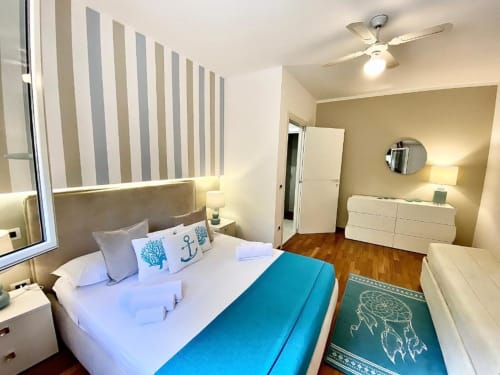 Camera luminosa a Mottola Apartments a Tropea con parete a righe, letto matrimoniale, plaid azzurro, cassettone bianco e