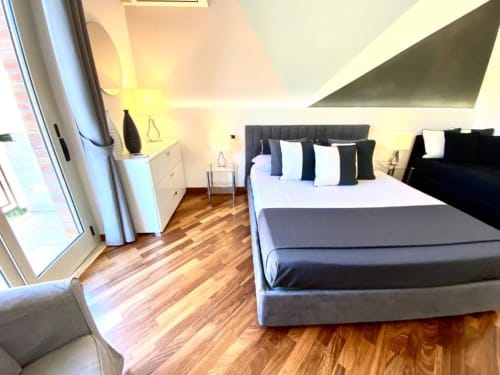 Camera da letto Superior moderna di Mottola Apartments a Tropea con letto matrimoniale, pavimenti in legno e balcone con vista giardino