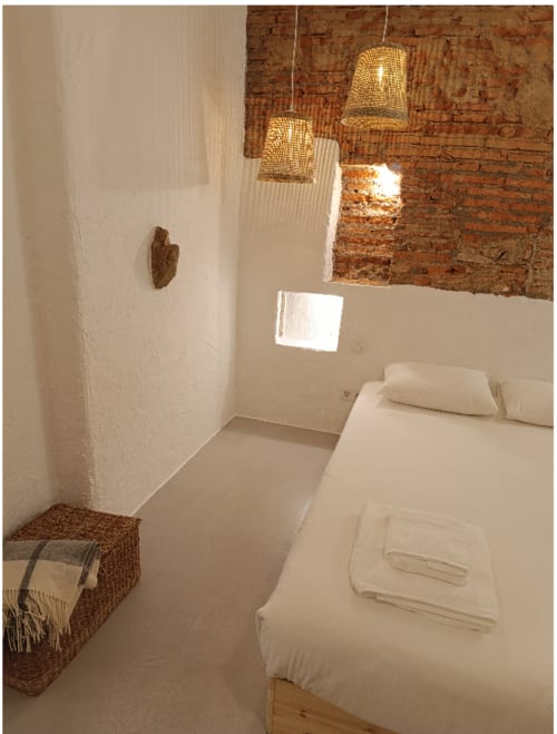 Quarto minimalista no apartamento Casas Velhinhas Calmaria, Estremoz, com paredes brancas, tijolos aparentes, luminárias de tecido trançado