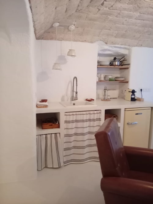 Kitchenete compacta no apartamento Casas Velhinhas com pia, fogão, geladeira creme, prateleiras abertas e cortina listrada
