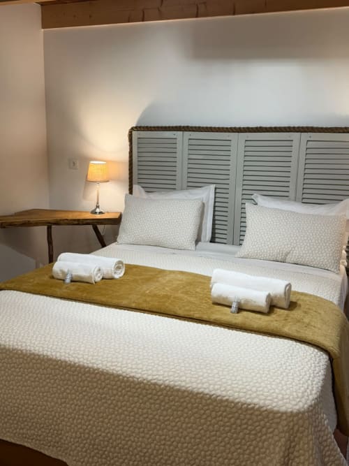 Quarto aconchegante no Refúgio do Nevoeiro com cama branca, cabeceira basculante, toalhas enroladas e luminária de cabeceira em São