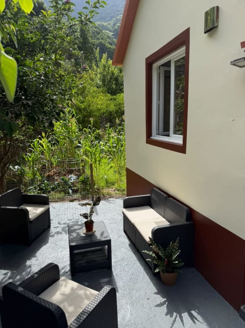 Pátio com vista para a montanha na pousada Refúgio do Nevoeiro, com móveis de fibra preta e exuberante jardim verde ao fundo
