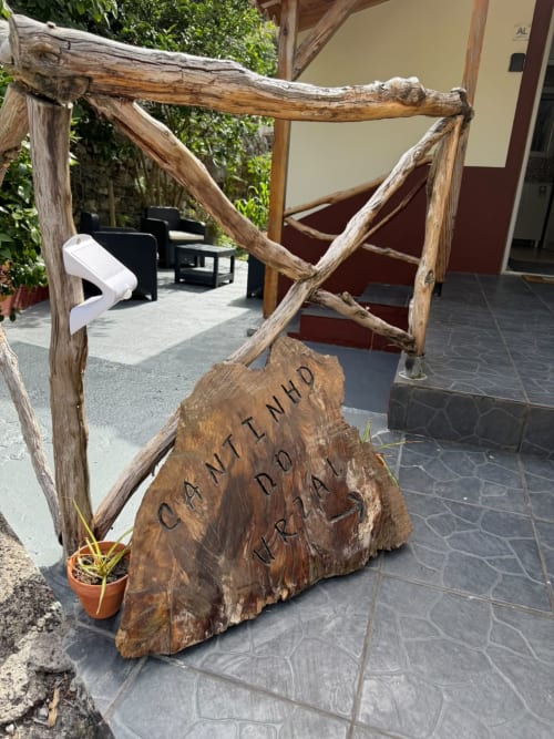 Placa rústica de madeira com a inscrição 'Cantinho do Urzal' na entrada da quinta Refúgio do Nevoeiro em São Vicente, Portugal