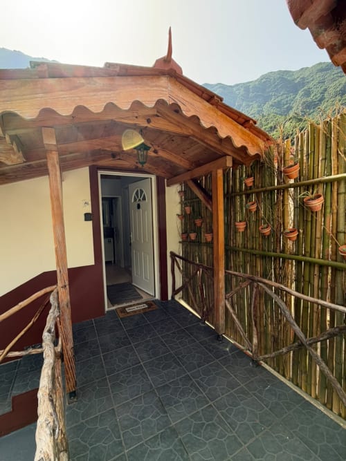 Pátio da cabana no Refúgio do Nevoeiro com pérgola de madeira, plantas em vasos na cerca e vistas da montanha em São Vicente.