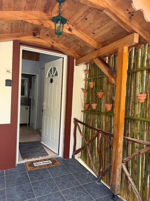 Entrada de pátio coberto da pousada Cantinho do Urzal em Refúgio do Nevoeiro com plantas em vasos e vigas de madeira