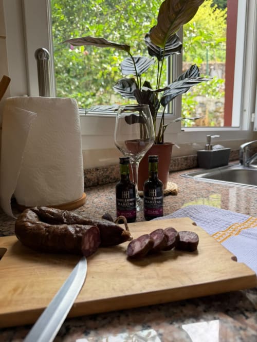 Balcão de cozinha rústica com carnes curadas fatiadas, garrafas de vinho da Madeira e plantas em vaso no Refúgio do Nevoeiro
