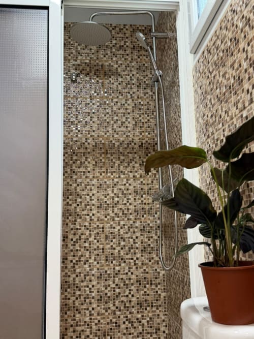 Banheiro moderno com revestimento de pastilhas em tons neutros na Pousada Refúgio do Nevoeiro, dotado de chuveiro tipo rainfall