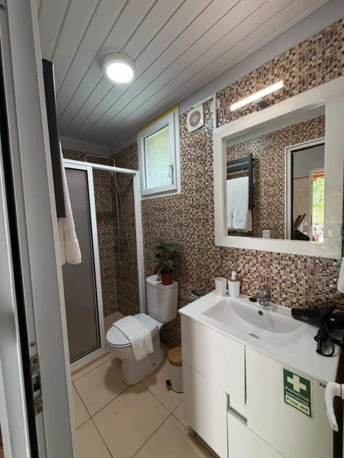 Banheiro moderno com azulejos mosaico marrom, pia branca, vaso sanitário e box na pousada Refúgio do Nevoeiro