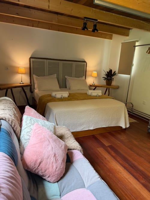 Quarto aconchegante da pousada Refúgio do Nevoeiro em São Vicente com cama queen, vigas de madeira e área de estar