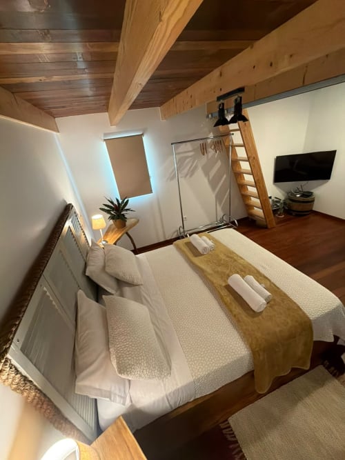 Quarto estilo loft moderno no Refúgio do Nevoeiro com vigas de madeira, cama com toalhas dobradas, TV e vistas da serra de São Vicente
