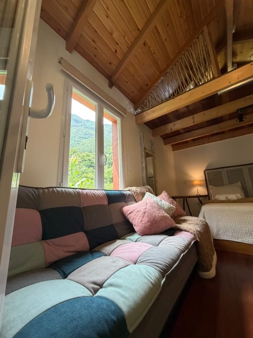 Quarto aconchegante na pousada Refúgio do Nevoeiro com cama colorida acolchoada, vistas da montanha, vigas de madeira e área de estar