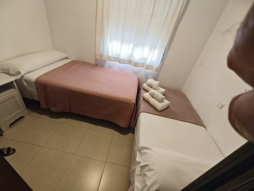 Dormitorio moderno en apartamento de Fuengirola con camas gemelas, colcha rosa, toallas limpias y cortinas translúcidas con luz natural
