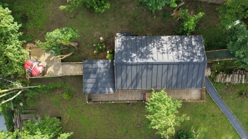 Vue aérienne du gîte Cœur de Lodge à Cramoisy, entouré d'une forêt verdoyante et d'une terrasse en bois avec toit en métal foncé