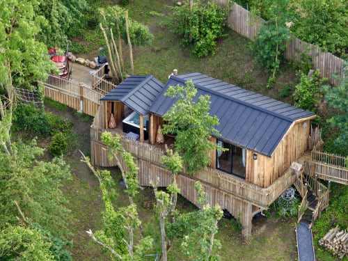 Cabane perchée Coeur de Lodge à Cramoisy avec toit noir, terrasse en bois et végétation forestière environnante