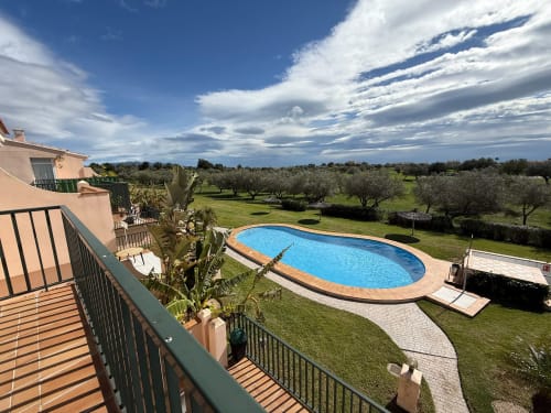 Vista desde el balcón de la piscina ovalada, jardines cuidados y olivares en la propiedad golfística Sant Jordi