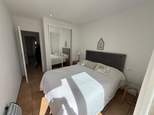 Dormitorio moderno con cabecera oscura, ropa de cama blanca, armario espejo y piso de baldosas en el apartamento Home Guardian Services