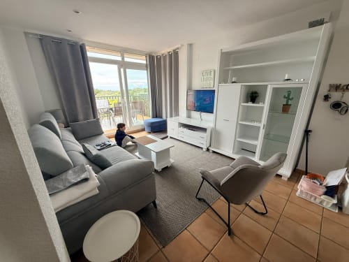 Moderno salón en Sant Jordi con vistas al golf, asientos grises, almacenamiento blanco, balcón y área de entretenimiento TV