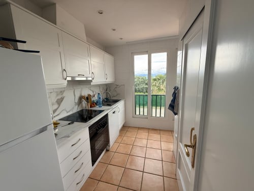 Cocina blanca moderna con salpicadero de mármol, azulejos de terracota y puertas con vista al jardín del apartamento Sant Jordi