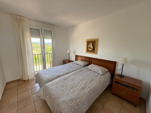 Habitación luminosa con camas gemelas, muebles de madera, balcón con vista al jardín y campo de golf en Home Guardian Services Sant