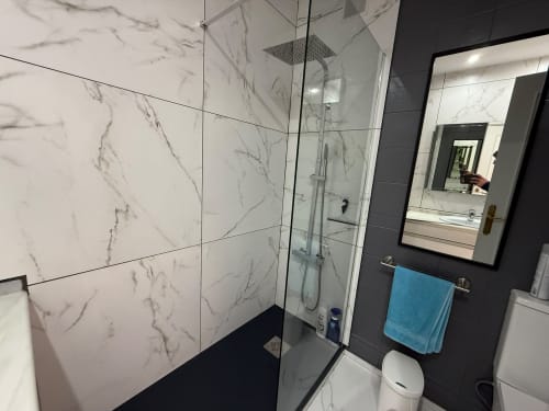 Baño moderno con azulejos efecto mármol, cabina de ducha cristal, paredes oscuras y espejo en apartamento Home Guardian Services