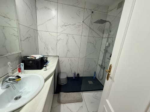 Baño moderno con azulejos de mármol, ducha de cristal, lavamanos blanco y plato de ducha negro en Home Guardian Services