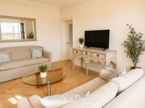 Elegant living room in luxury Dorset coastal chalet with cream sofa, glass coffee table, flat-screen TV on ornate desk, and