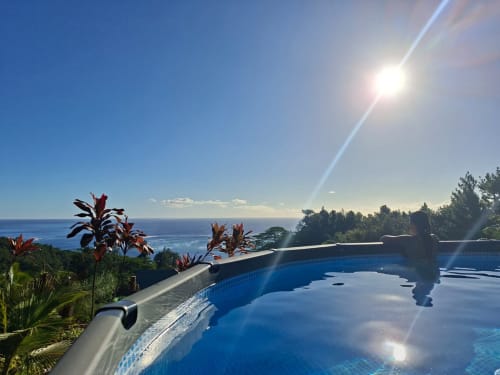 Piscine à débordement face à l'océan bleu de Fare Tihi Moana à Raiatea, Polynésie française, avec végétation tropicale et ciel ensoleillé