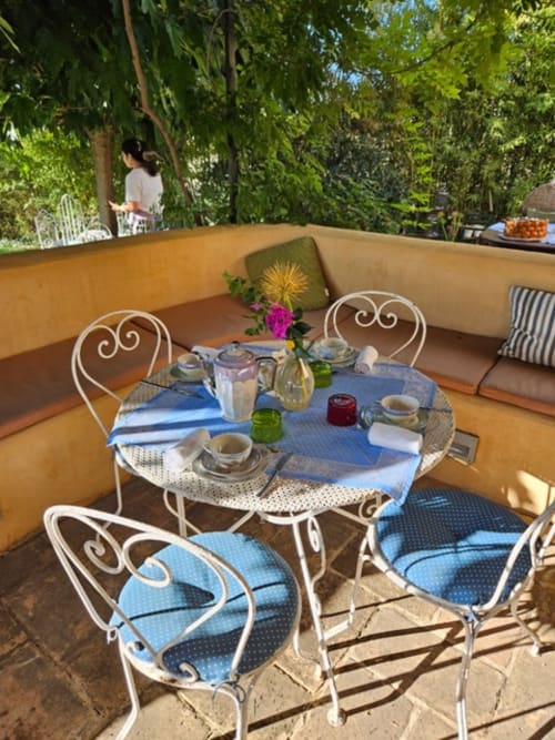 Espace repas en terrasse au Clos Bb avec chaises blanches ornementales, nappe bleue, fleurs fraîches à Saint-Cyr