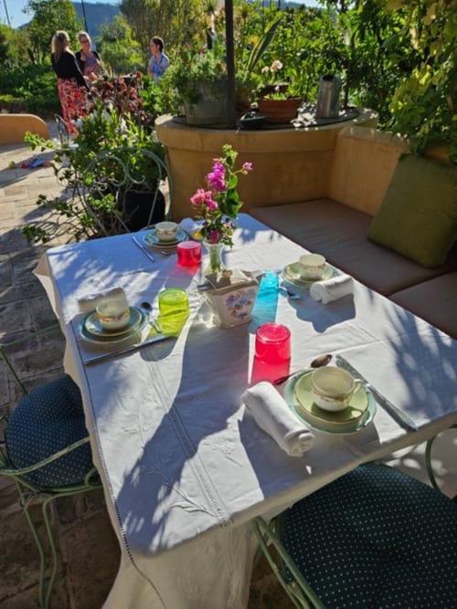 Salle à manger en plein air au Clos BB avec table élégamment dressée, fleurs roses et jardins luxuriants à Saint-Cyr sur Mer