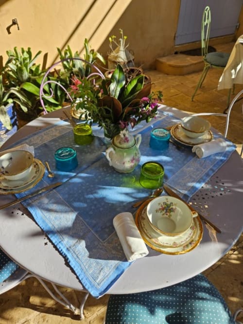 Élégante table dressée au Clos Bb avec porcelaine fleurie, fleurs fraîches en vases de verre et linges bleus à Saint-Cyr sur Mer