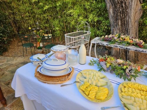 Aménagement de salle à manger extérieure chez Clos BB avec nappe blanche, couverts, plateaux de fruits frais et compositions florales
