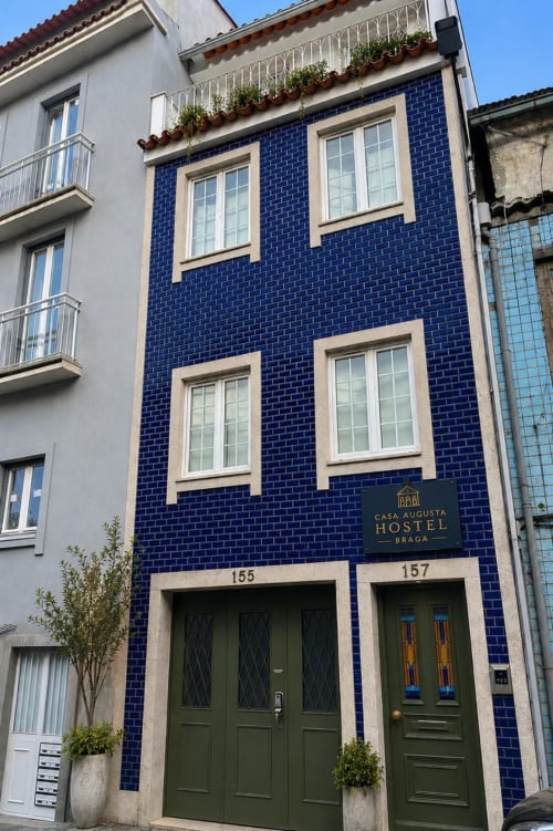 Fachada exterior da Casa Augusta Hostel Braga com tijolos azuis, duas portas verdes e molduras em pedra creme
