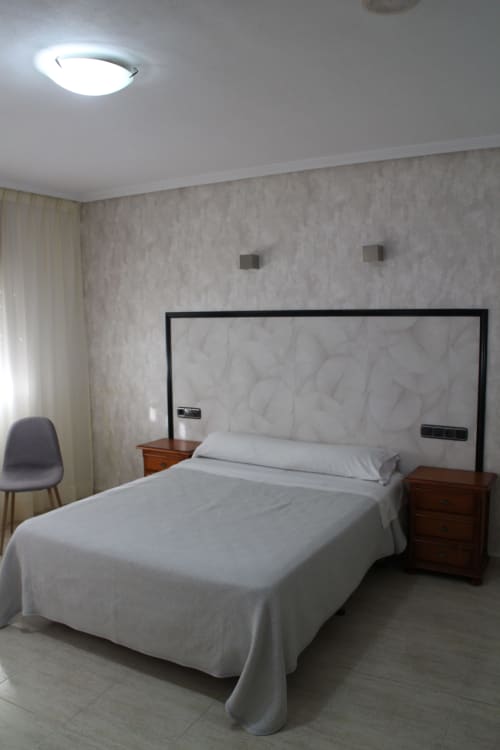 Habitación moderna del Mesón Hotel El 21 en Níjar con ropa de cama blanca, mesillas de madera y cabecero de diseño contemporáneo