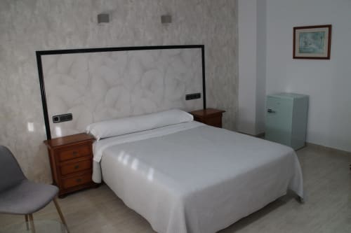 Luminosa habitación doble en Mesón Hotel El 21 de Níjar con ropa de cama blanca, mesita de noche de madera y refrigerador menta