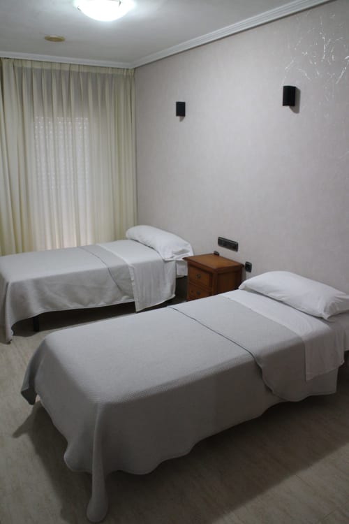 Habitación doble en Mesón Hotel El 21 de Níjar con dos camas, ropa blanca, cortinas y altavoces de pared