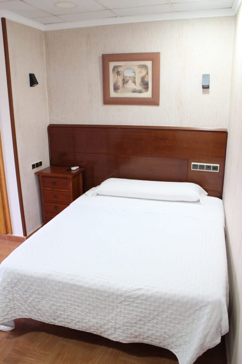 Habitación doble en Mesón Hotel El 21 de Níjar con cama de madera, ropa de cama blanca y cabecero de madera oscura con amenidades integradas