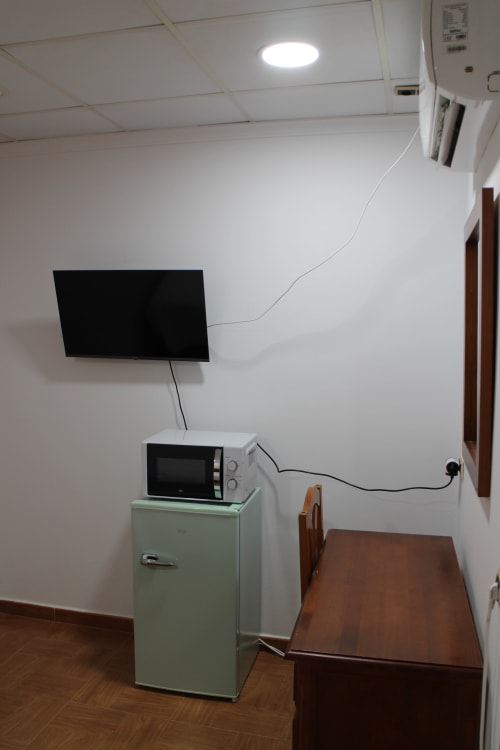 Habitación del Mesón Hotel El 21 con televisor de pantalla plana, microondas, refrigerador vintage y mesa de madera