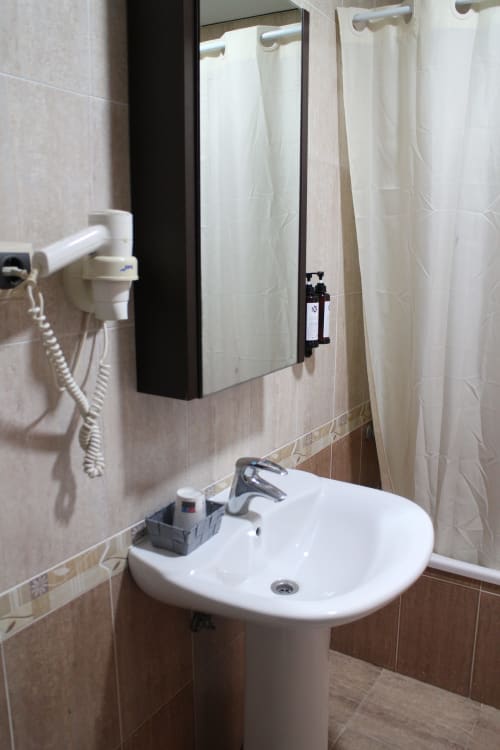 Baño moderno del Mesón Hotel El 21 en Níjar con lavamanos de pedestal blanco, espejo y cortina de ducha