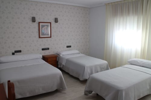 Habitación triple del Mesón Hotel El 21 en Níjar con tres camas individuales, mesita de noche de madera, papel tapiz floral y ventanas luminosas