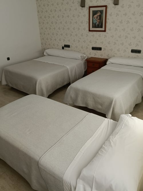 Habitación triple del Mesón Hotel El 21 en Níjar con tres camas individuales y papel tapiz floral clásico