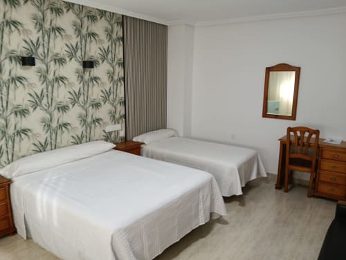 Habitación triple en Mesón Hotel El 21 de Níjar con dos camas, muebles de madera y papel pintado botánico