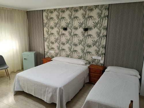 Habitación triple en Mesón Hotel El 21 de Níjar con dos camas, mesillas de madera y papel pintado botánico