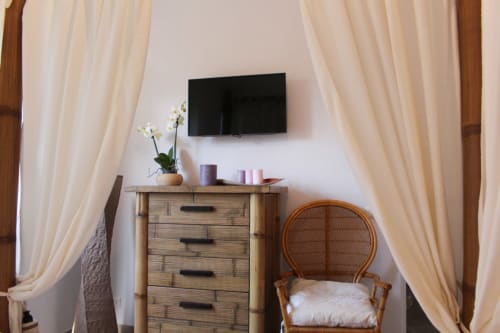 Camera LILLA Suite presso MAISON TIZI con TV a parete, cassettone in legno, sedia in rattan, tende color crema e vista sul giardino