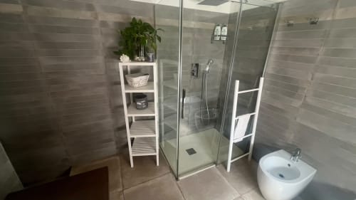 Bagno moderno della Suite LILLA di MAISON TIZI con doccia walk-in, mensole bianche, pianta in vaso e bidet a Fiumicino Roma