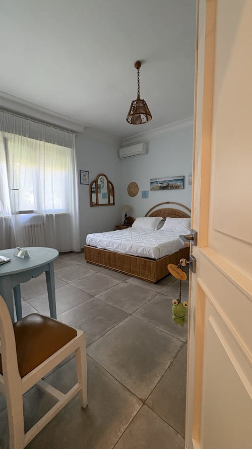 Camera Acquamarina Suite presso MAISON TIZI con letto in vimini, biancheria bianca, pavimentazione in piastrelle e finestre con vista giardino